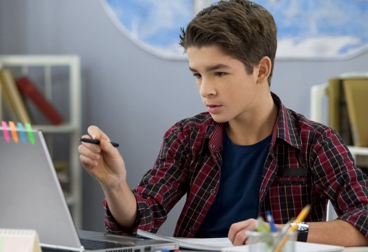 Male child doing homework in room using e-book on laptop, contemporary education