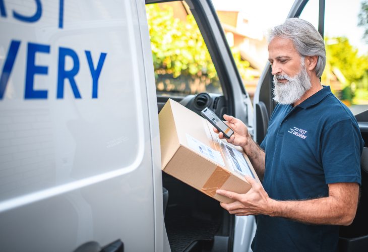 Mature delivery man with beard delivering the package to client, scanning the label.