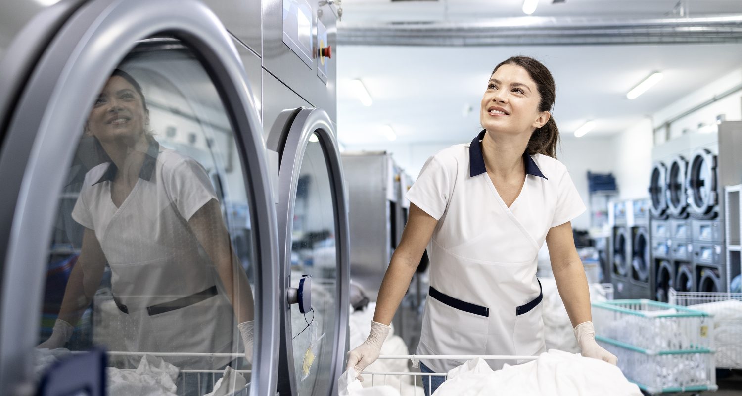 Smiling female cleaner preparing laundry for washing in dry cleaning service.